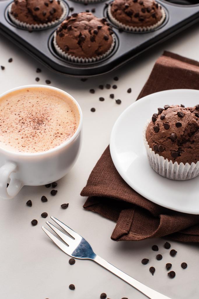 muffins de chocolate fresco em lata de muffin, guardanapo marrom com placa perto de café e garfo
 - Foto, Imagem