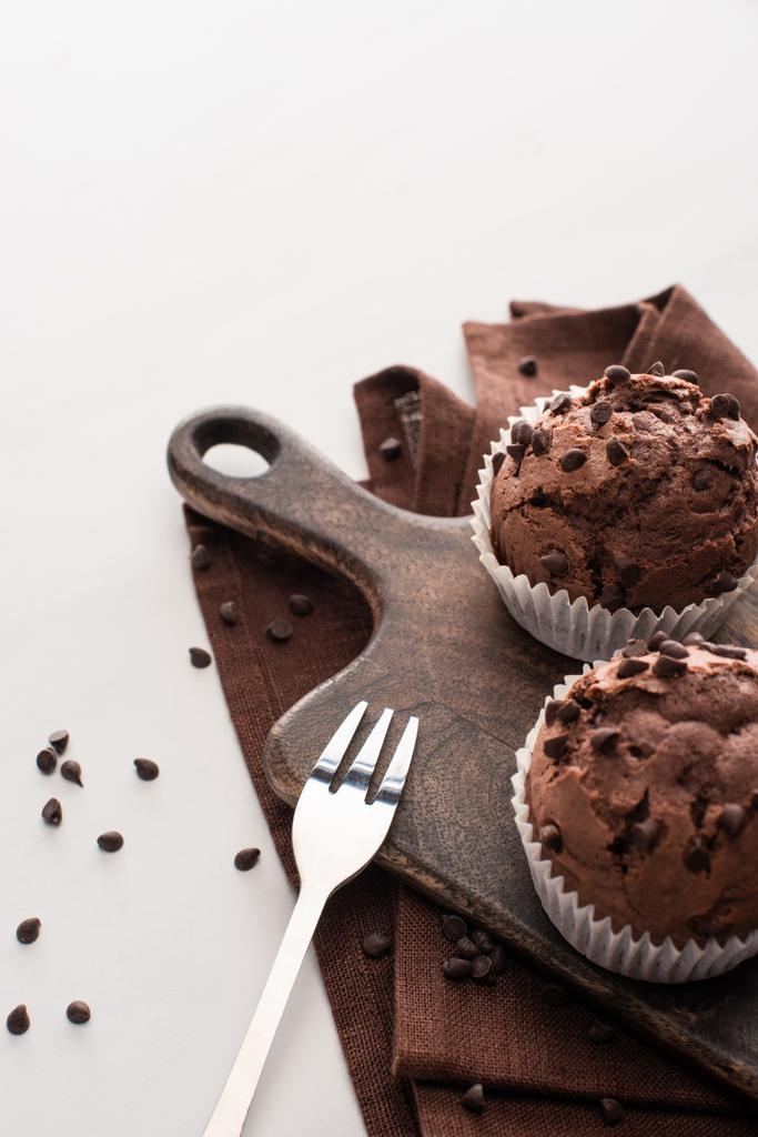 fresh chocolate muffins on wooden cutting board on brown napkin with fork - Fotoğraf, Görsel
