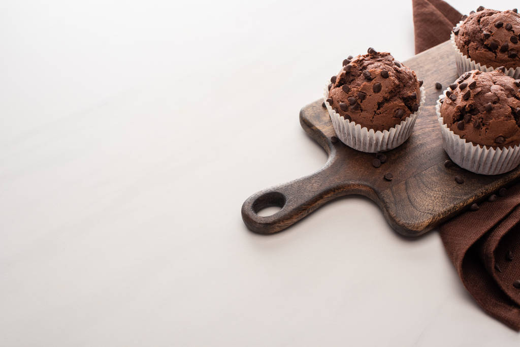 magdalenas de chocolate fresco en la tabla de cortar de madera cerca de la servilleta marrón
 - Foto, Imagen