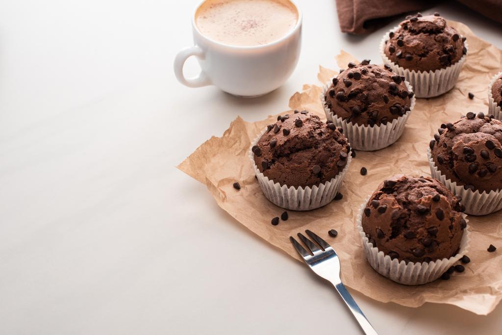 fresh chocolate muffins on parchment paper with fork near coffee - Fotoğraf, Görsel