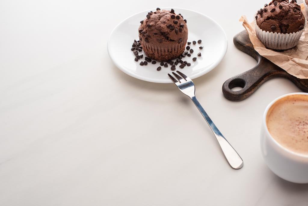 fresh chocolate muffins on wooden cutting board and plate with fork near coffee - Photo, Image