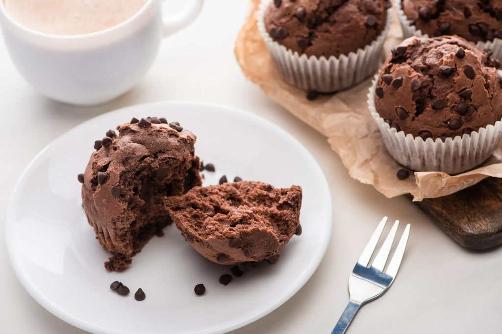 fresh chocolate muffins on wooden cutting board near plate, fork and coffee - 写真・画像