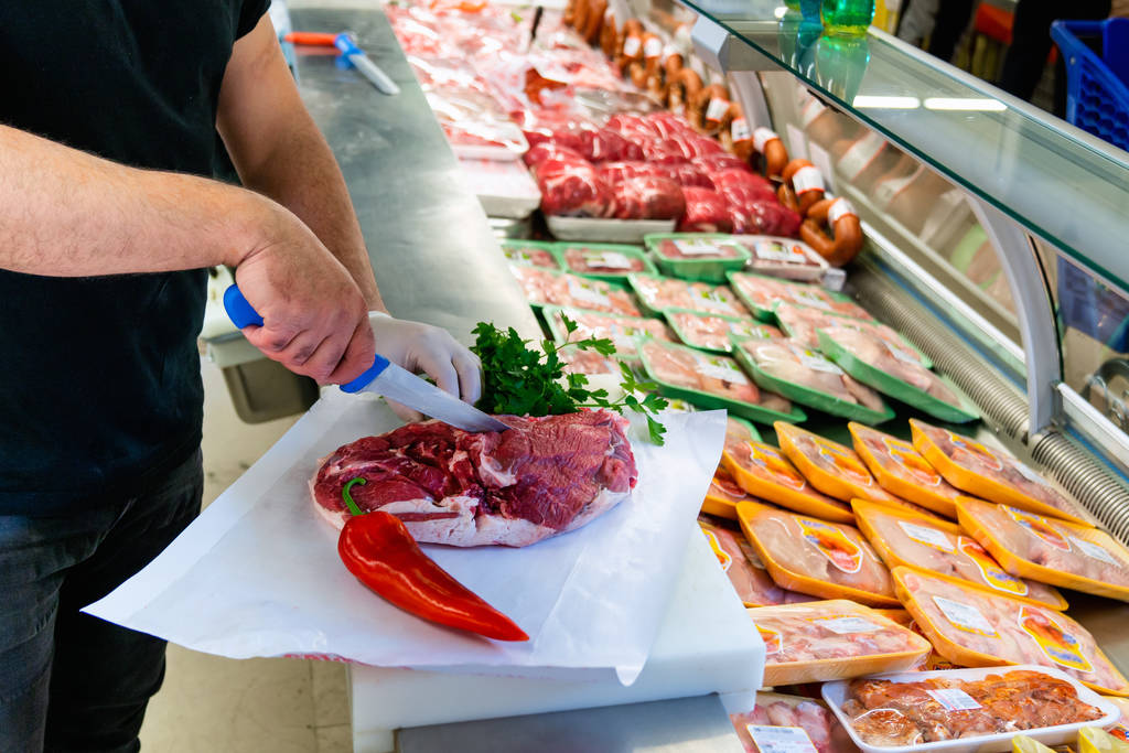 Metzger arbeitet in einer Fleischabteilung eines Marktes und schneidet Fleisch. Essen und kulinarisches Konzept. - Foto, Bild