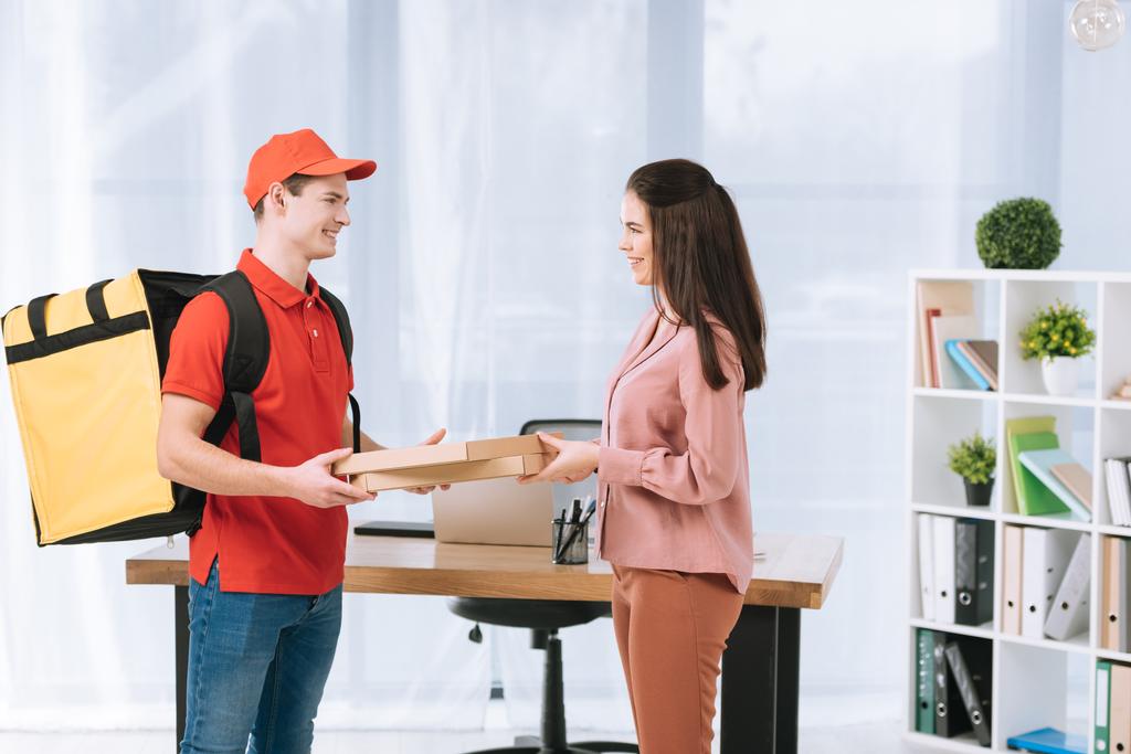 Ofisteki gülümseyen iş kadınına pizza kutuları dağıtan teslimatçının yan görüntüsü. - Fotoğraf, Görsel