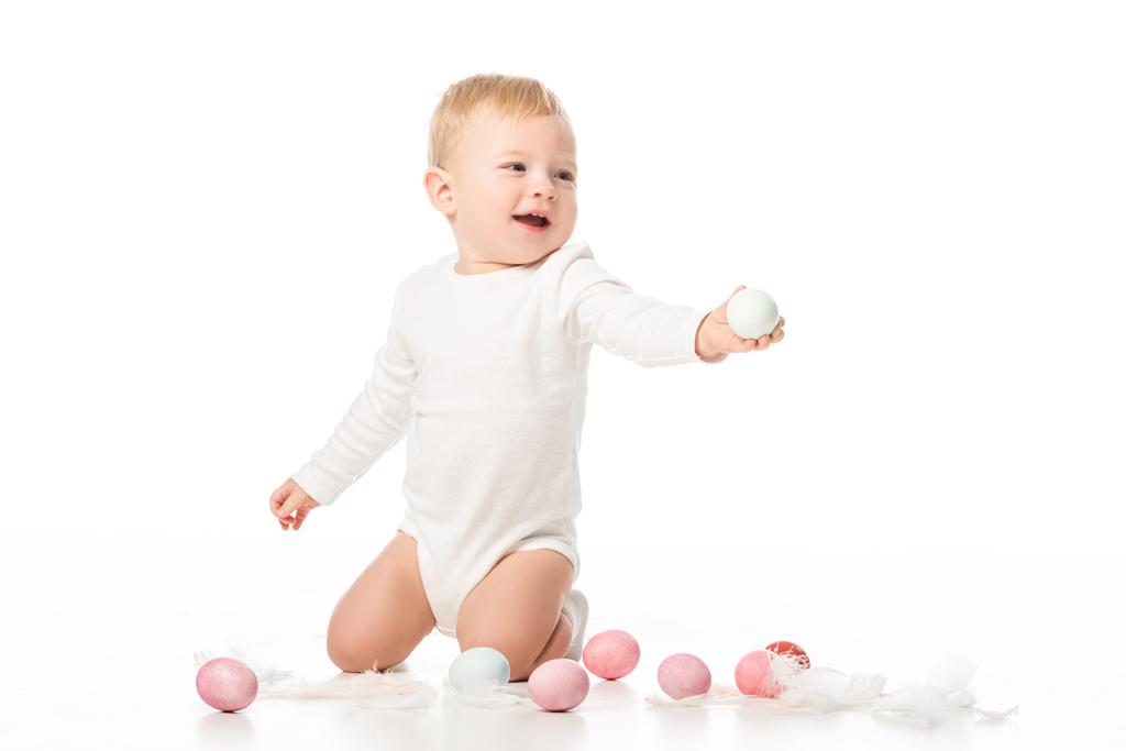 Child next to easter eggs and feathers on white background - Photo, Image