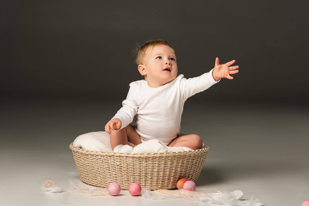 Child with outstretched hand looking up, sitting in basket on black background - Photo, Image