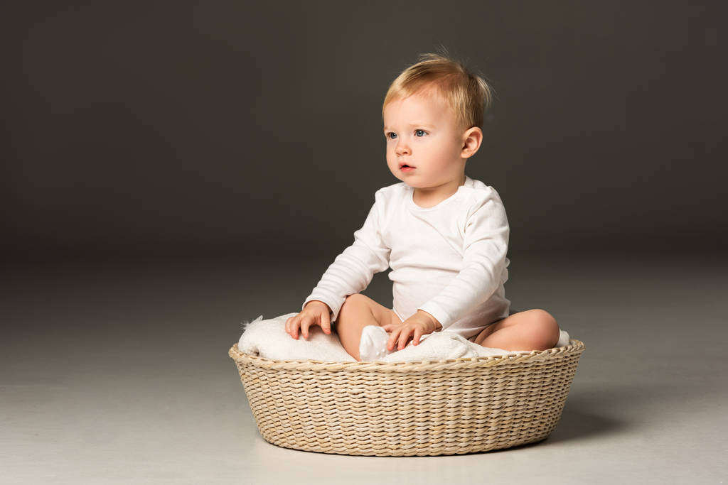 Cute boy sitting on blanket in basket on black background - Photo, Image