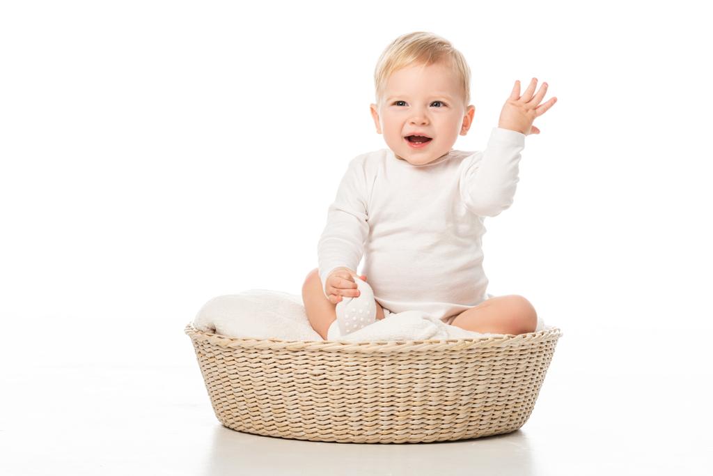 Lapsi, jolla on kohotettu käsi ja avoin suu, istuu huopa korissa valkoisella taustalla
 - Valokuva, kuva