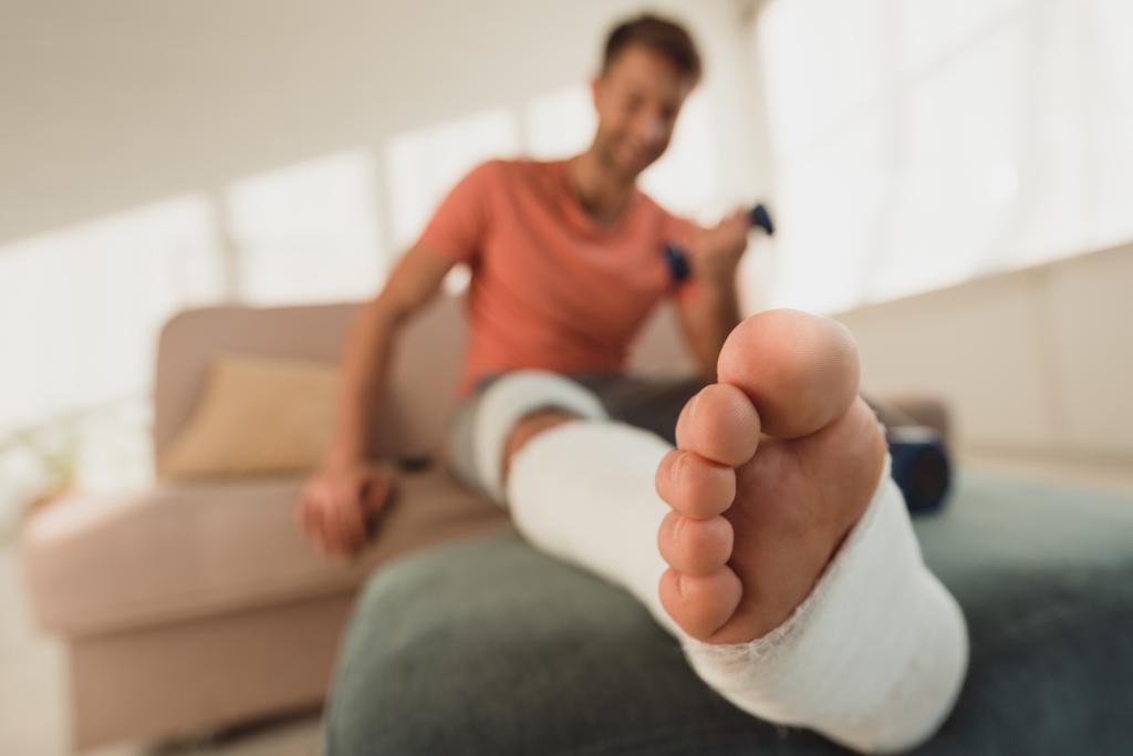 Szelektív fókusz a törött láb férfi súlyzóval a kanapén - Fotó, kép