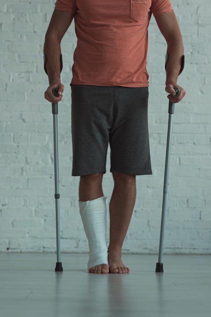 Vista recortada del hombre con pierna en vendaje de yeso que sostiene muletas
  - Foto, Imagen