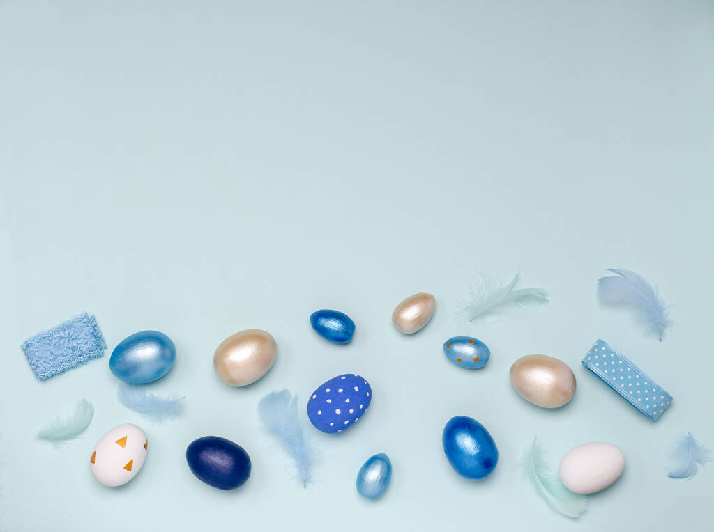 Huevos de Pascua en tonos azules con plumas y cintas azules sobre un fondo azul con espacio para copiar
. - Foto, Imagen