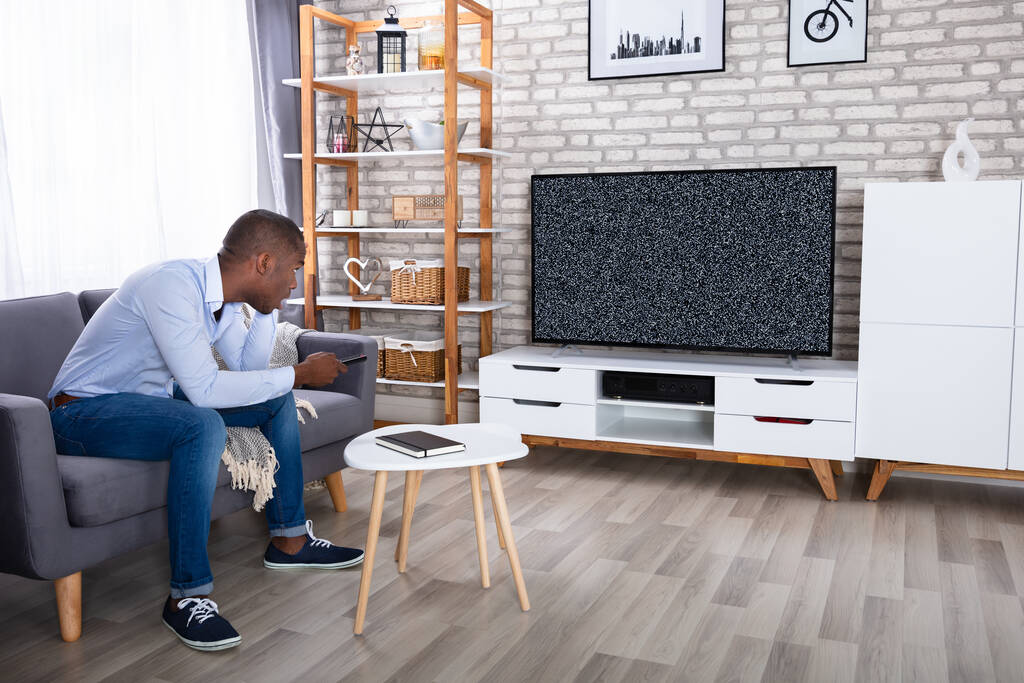 Africano homem sentado na cama olhando para a televisão sem sinal
 - Foto, Imagem
