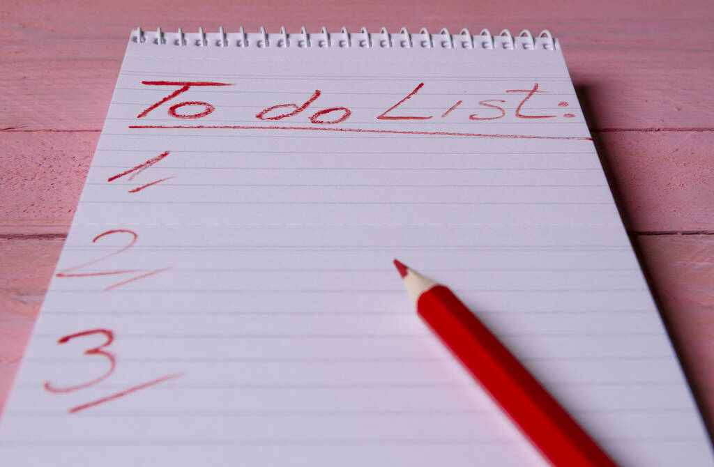 Cuaderno espiral con una lista de cosas por hacer escrito con un lápiz rojo en él, sobre una mesa de madera rosa
 - Foto, Imagen