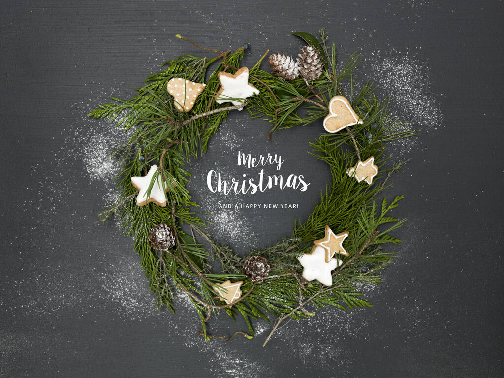 grüner Weihnachtskranz auf schwarzem Hintergrund mit vielen verschiedenen Weihnachtsartikeln und Schriftzug Frohe Weihnachten - Foto, Bild