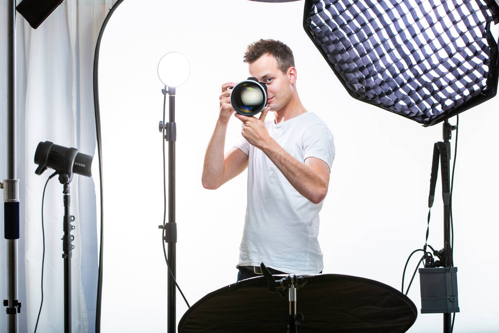 Fiatal profi fotós digitális fényképezőgéppel - DSLR és egy hatalmas teleobjektívvel az ő jól felszerelt stúdió, fotózás (színes tónusú kép - Fotó, kép
