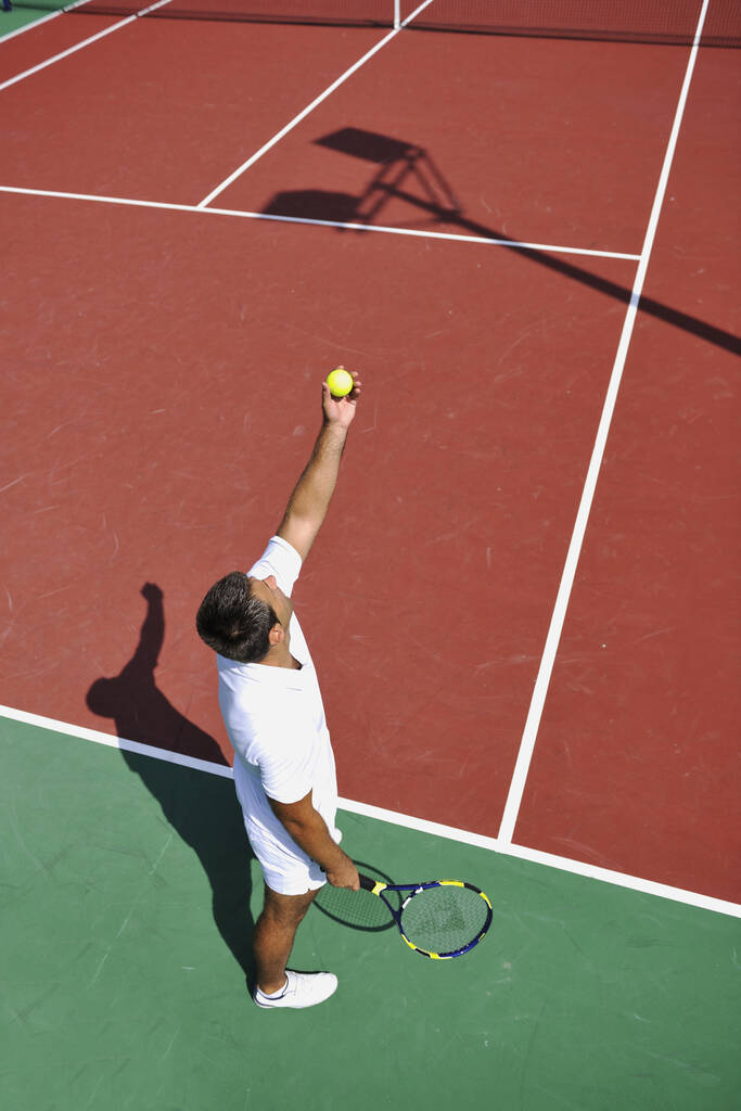 Giovane giocare a tennis all'aperto sul campo da tennis arancione al mattino presto
 - Foto, immagini