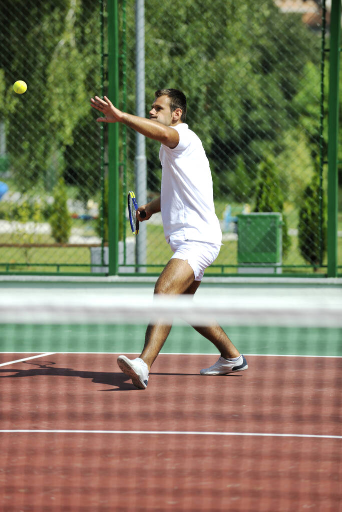 Jeune homme jouer au tennis en plein air sur un court de tennis orange tôt le matin
 - Photo, image
