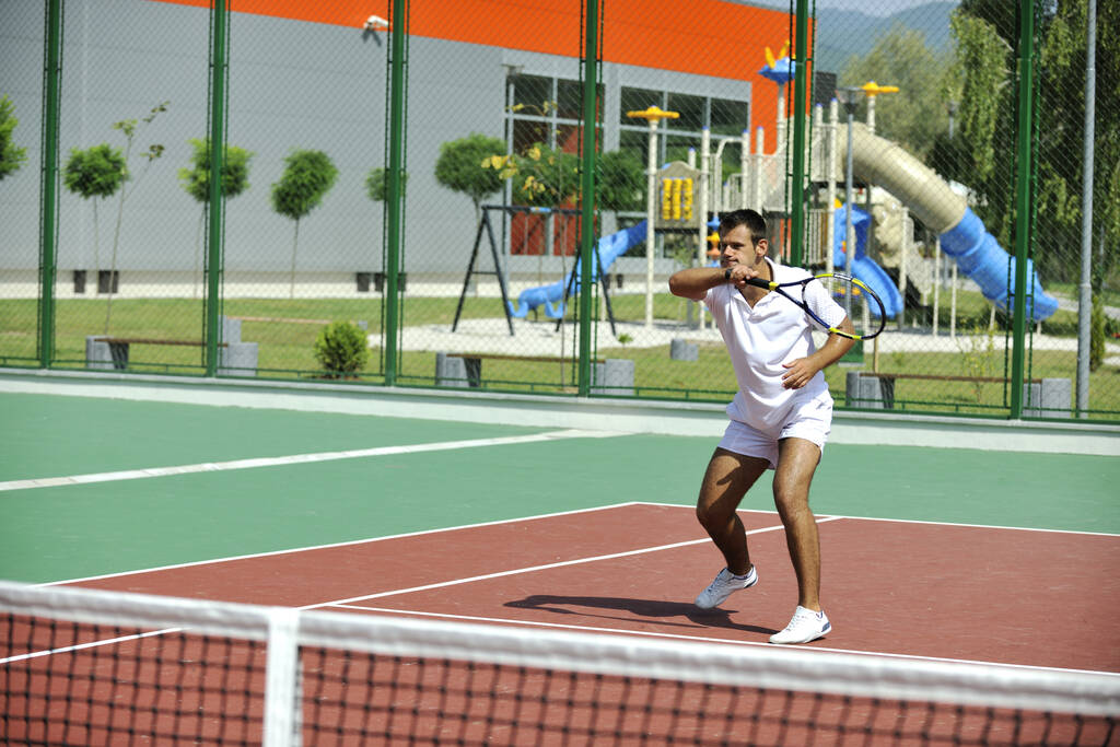 Jovem joga tênis ao ar livre no campo de ténis laranja no início da manhã
 - Foto, Imagem