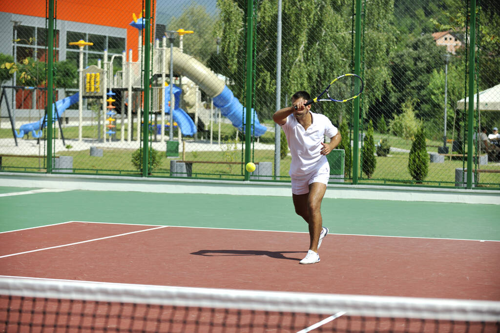 Молодий чоловік грає в теніс на відкритому повітрі на помаранчевому тенісному корті рано вранці
 - Фото, зображення