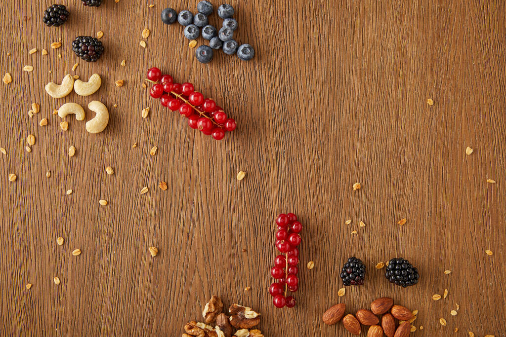 Bovenaanzicht van bosbessen, rode bessen, walnoten, amandelen, cashewnoten op houten ondergrond - Foto, afbeelding