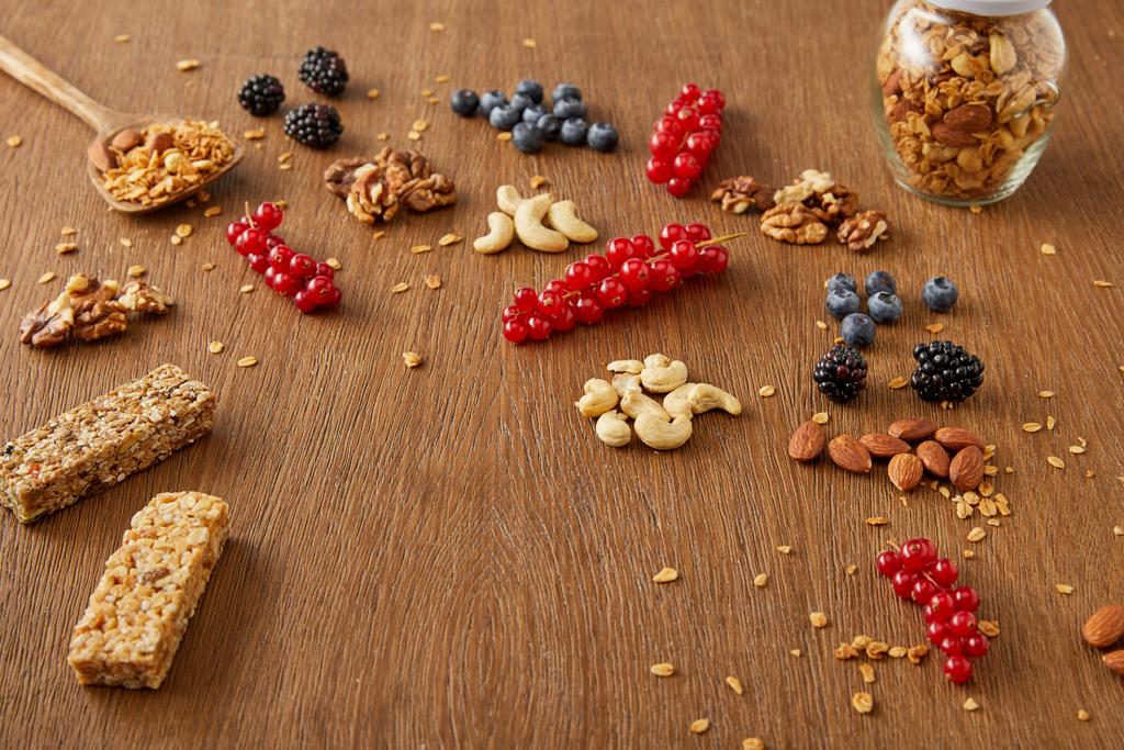 Potje granola naast bessen, noten, graanrepen op houten ondergrond - Foto, afbeelding