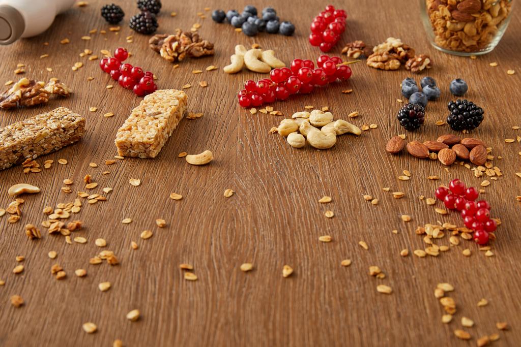 grosellas rojas, arándanos, nueces, almendras, anacardos, copos de avena y barras de cereales sobre fondo de madera
 - Foto, Imagen