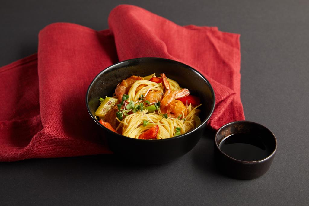 nouilles aux crevettes et légumes dans un bol près de la sauce soja sur une serviette rouge sur fond noir
 - Photo, image