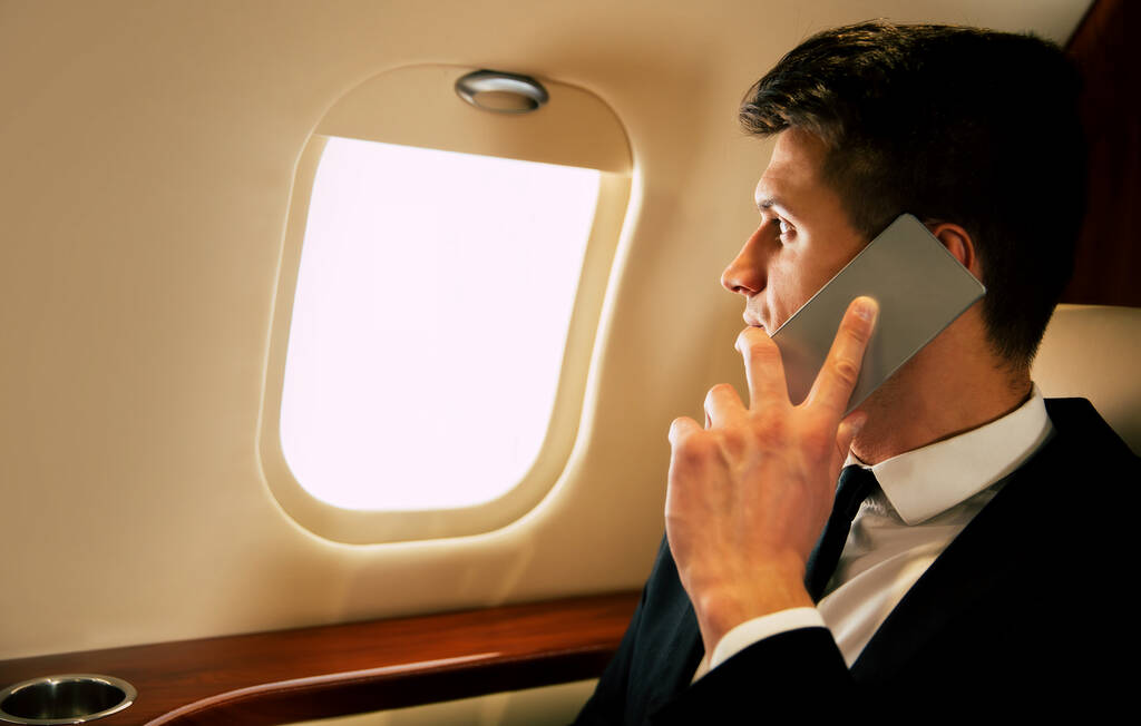 fiatal üzletember a gépen beszél okostelefonon  - Fotó, kép