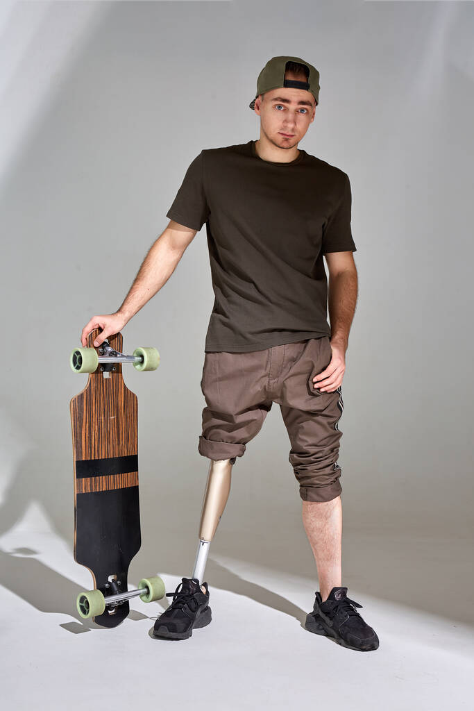 Gehandicapte jongeman met beenprothese met longboard skateboard op witte achtergrond. Zonlicht. - Foto, afbeelding