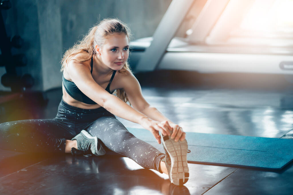 Flexibele jonge vrouw stretching haar rechterbeen in gym.Sportieve vrouw stretching in de sportschool. - Foto, afbeelding