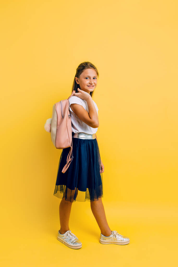Portrait of a smiling little schoolgirl with a backpack on a yel - Photo, Image