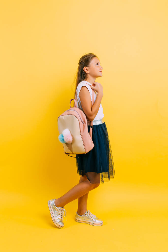 Portrait of a smiling little schoolgirl with a backpack on a yellow background - Photo, Image