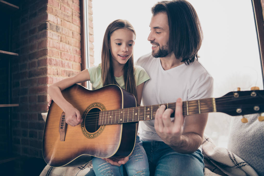 Photo of little funny adorable pretty lady and her handsome young daddy sit window sill hold acoustic guitar teaching new song part spend weekend time house room indoors - Photo, Image
