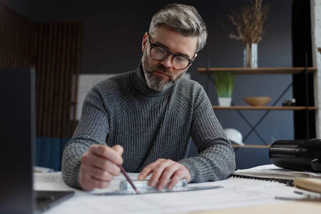 Interior designer working in office with blueprints.Engineer inspect architectural plan, sketching a construction project.Portrait of handsome bearded man at workplace. Business construction concept - Photo, Image