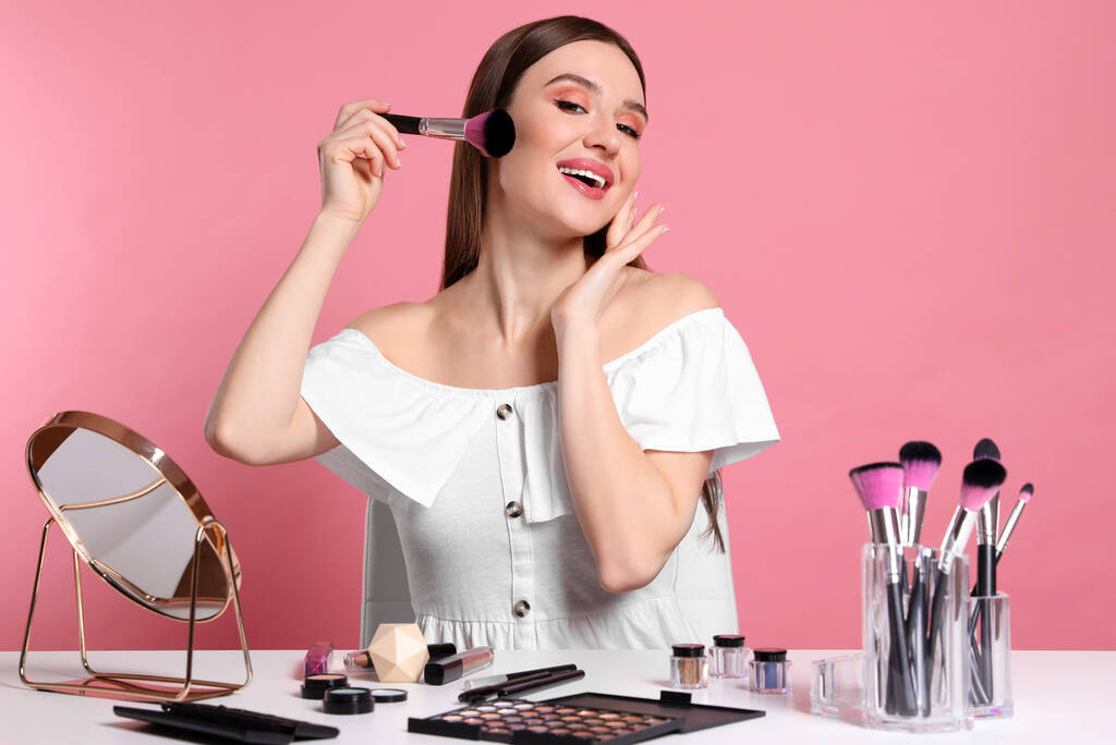 Schoonheid blogger doen make-up op roze achtergrond - Foto, afbeelding