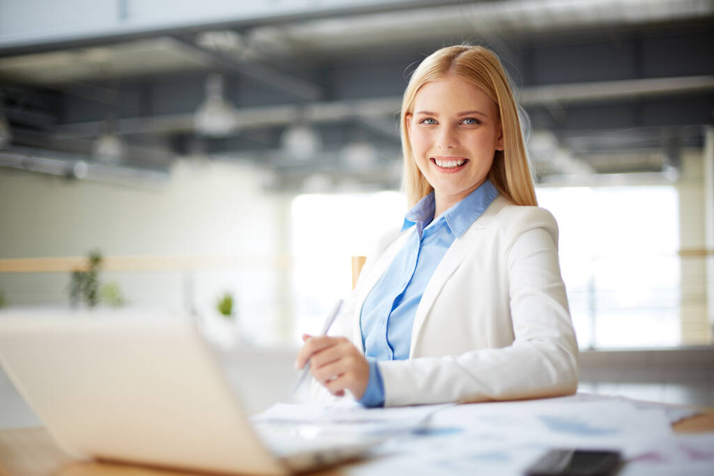Young businesswoman sitting at workplace in office and looking at camera - Photo, Image