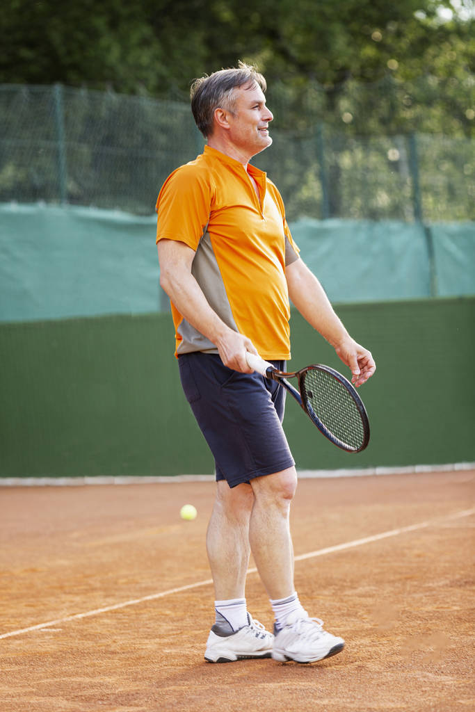 Een man speelt tennis op het veld op een zonnige dag. Gezondheid en activiteit. - Foto, afbeelding