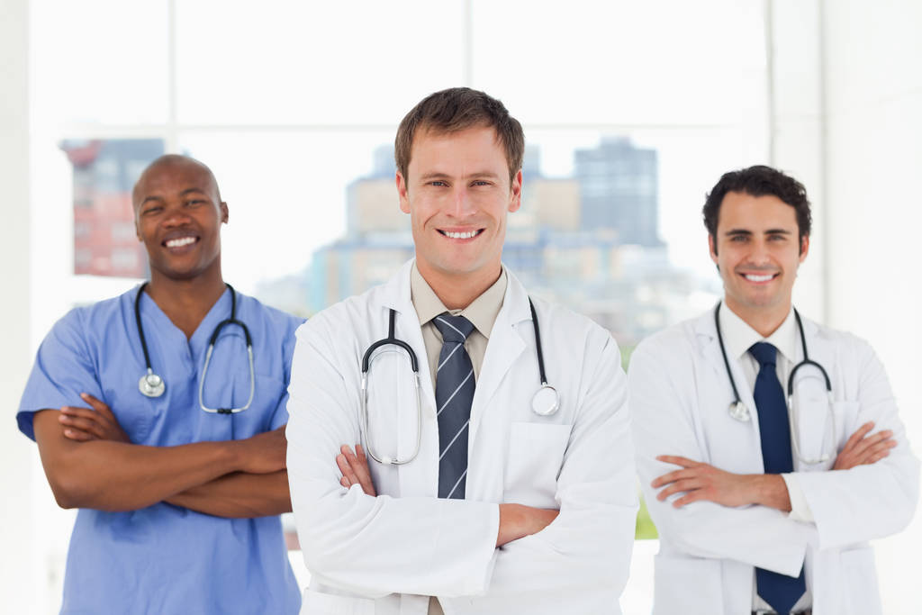 Χαμογελώντας γιατροί με διπλωμένα χέρια στέκεται μπροστά από ένα παράθυρο - Φωτογραφία, εικόνα