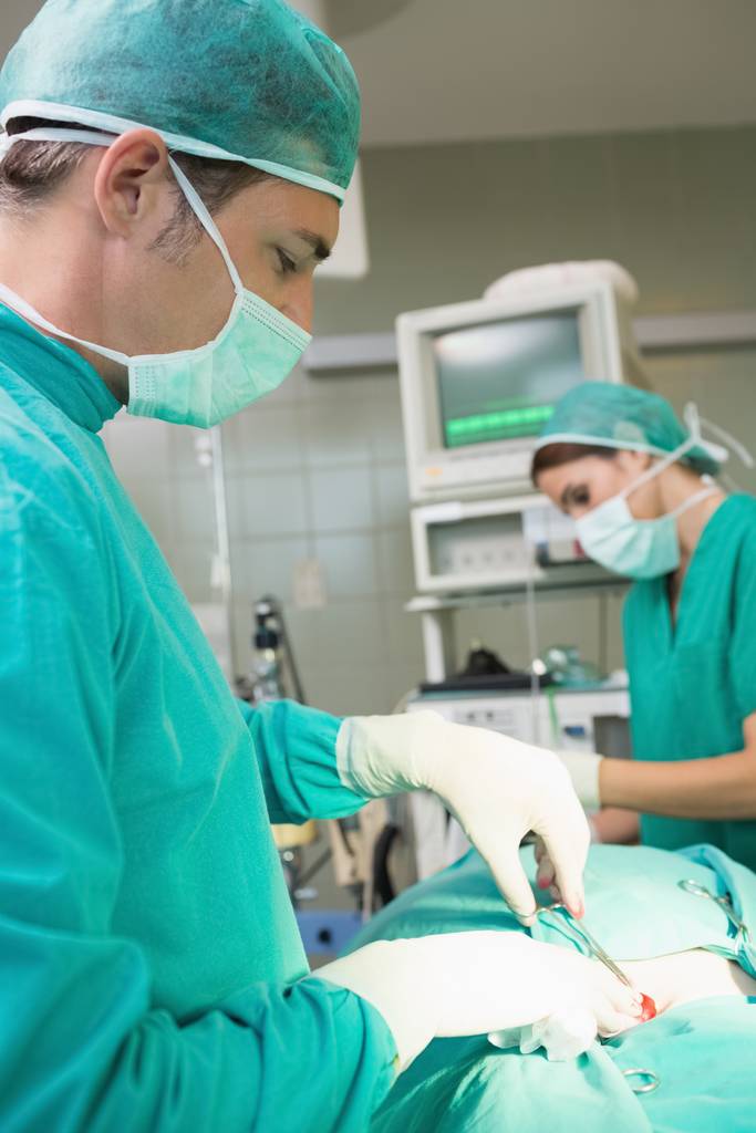 Detailní záběr mužského chirurga pomocí nůžek na operačním sále - Fotografie, Obrázek