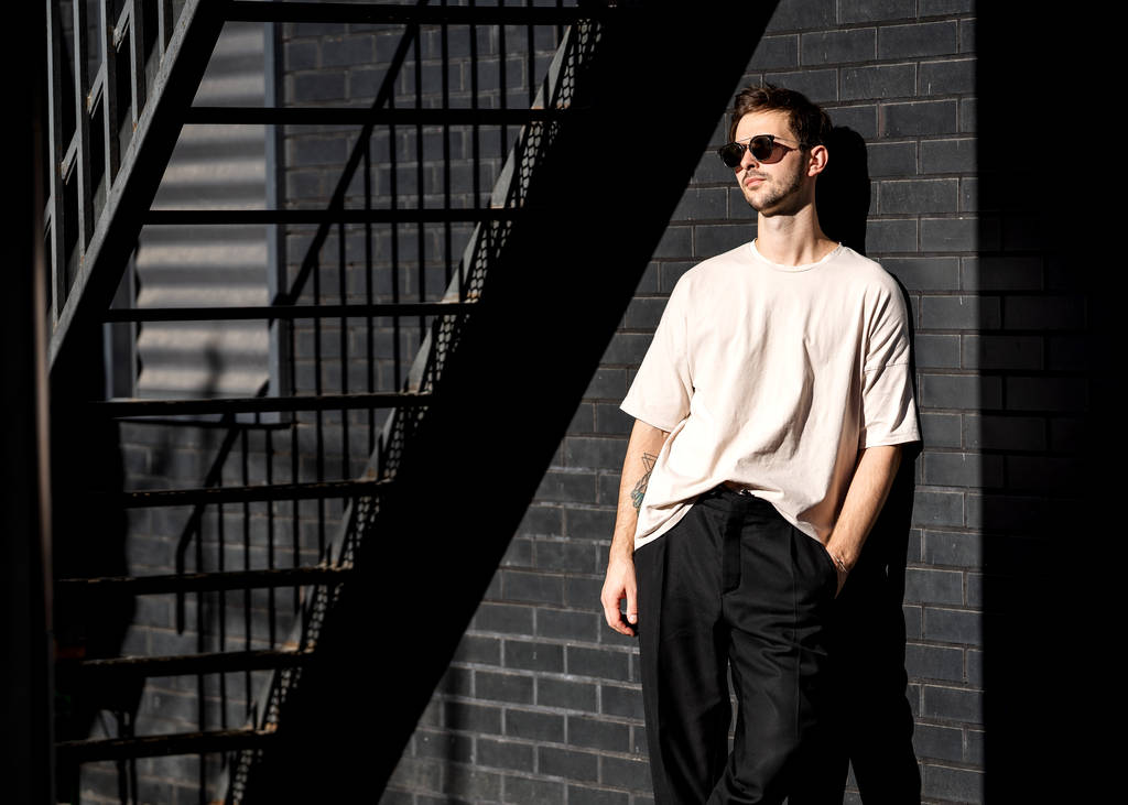 mode man staat poseren in de buurt van een zwarte baksteen muur in een zonnebril - Foto, afbeelding