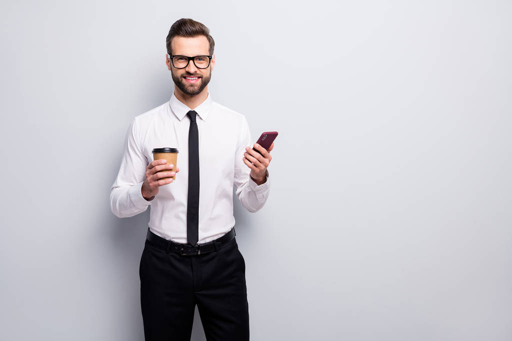 Portret van positieve advocaat ondernemer man houden cafeïne drank mok gebruik mobiele telefoon genieten sociale media bloggen dragen witte shirt zwarte broek ontspannen geïsoleerde grijze kleur achtergrond - Foto, afbeelding