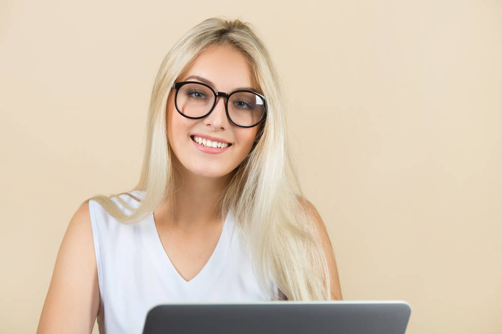 hermosa mujer joven en gafas sobre un fondo beige con un ordenador portátil
 - Foto, imagen