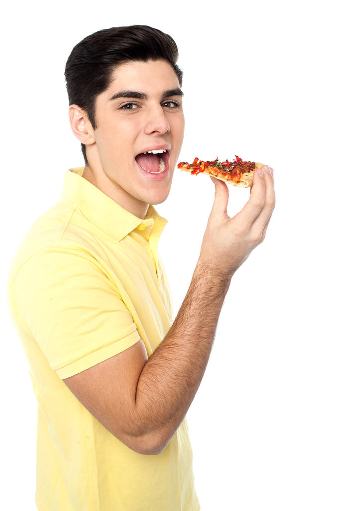 Красивий молодий чоловік зараз насолоджується шматочком піци
. - Фото, зображення