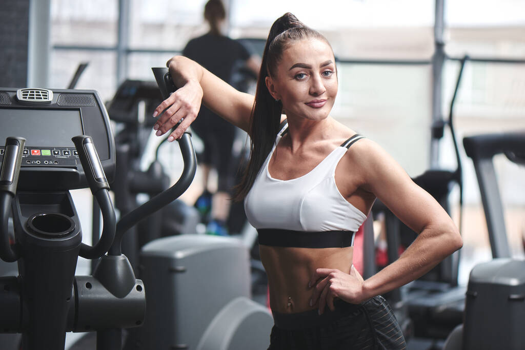 starke sexy brünette Frau mit Fitness muskulösen Körper posiert in der Nähe von Geräten im Fitnessstudio, Konzept der Sporternährung und Nahrungsergänzungsmittel - Foto, Bild
