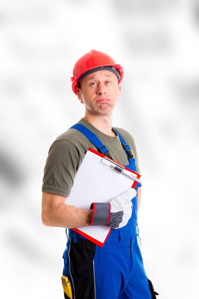 jeune ouvrier en dungarees bleues avec presse-papiers à l'air sceptique
 - Photo, image