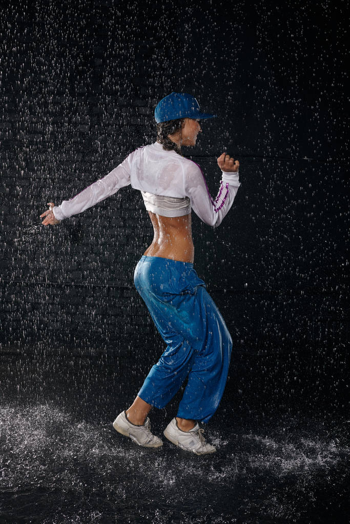 黒い背景に雨の下で美しい少女が水の中で踊る。モダンダンス. - 写真・画像