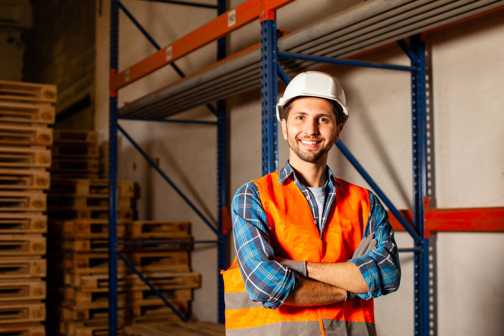 Confident handsome worker in protective hardhat and uniform at the warehouse of a industrial manufacturing - 写真・画像