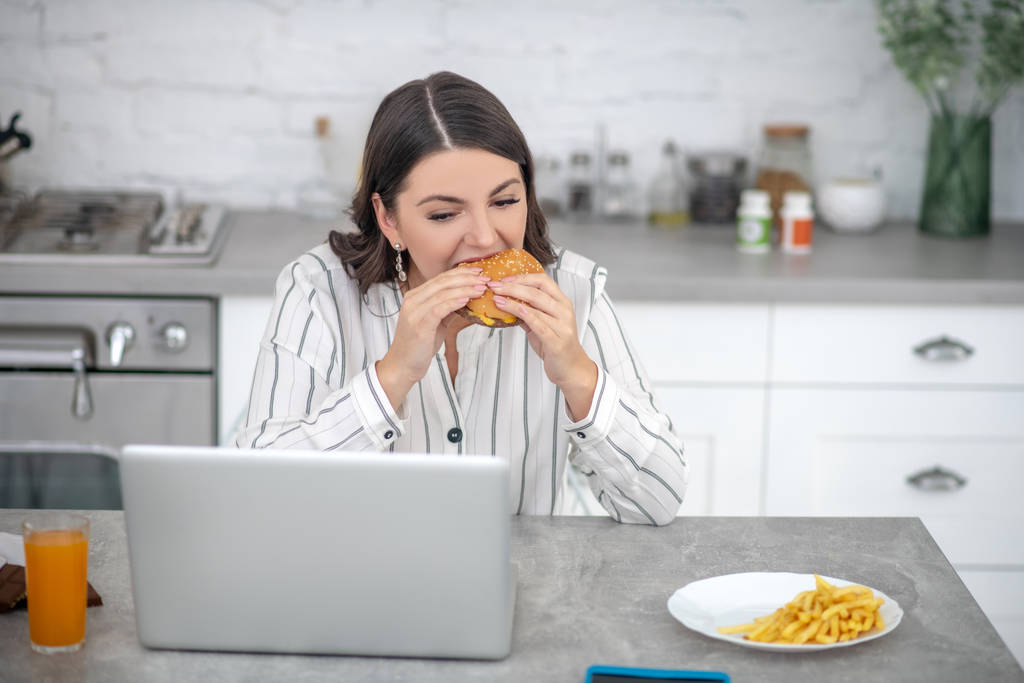 Tumma tukka nainen raidallinen pusero syö hampurilainen
 - Valokuva, kuva