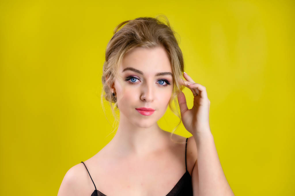 The concept of cosmetics, fashion and style. Glamorous beauty portrait of a pretty blonde model with excellent makeup and a beautiful hairstyle on a yellow background in the studio. - 写真・画像