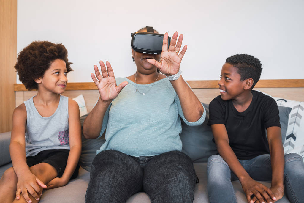 Grootmoeder en kleinkinderen spelen samen met VR bril. - Foto, afbeelding